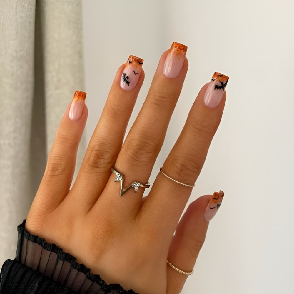 Faded orange Halloween nails with bat designs – classic Halloween color scheme nail art.